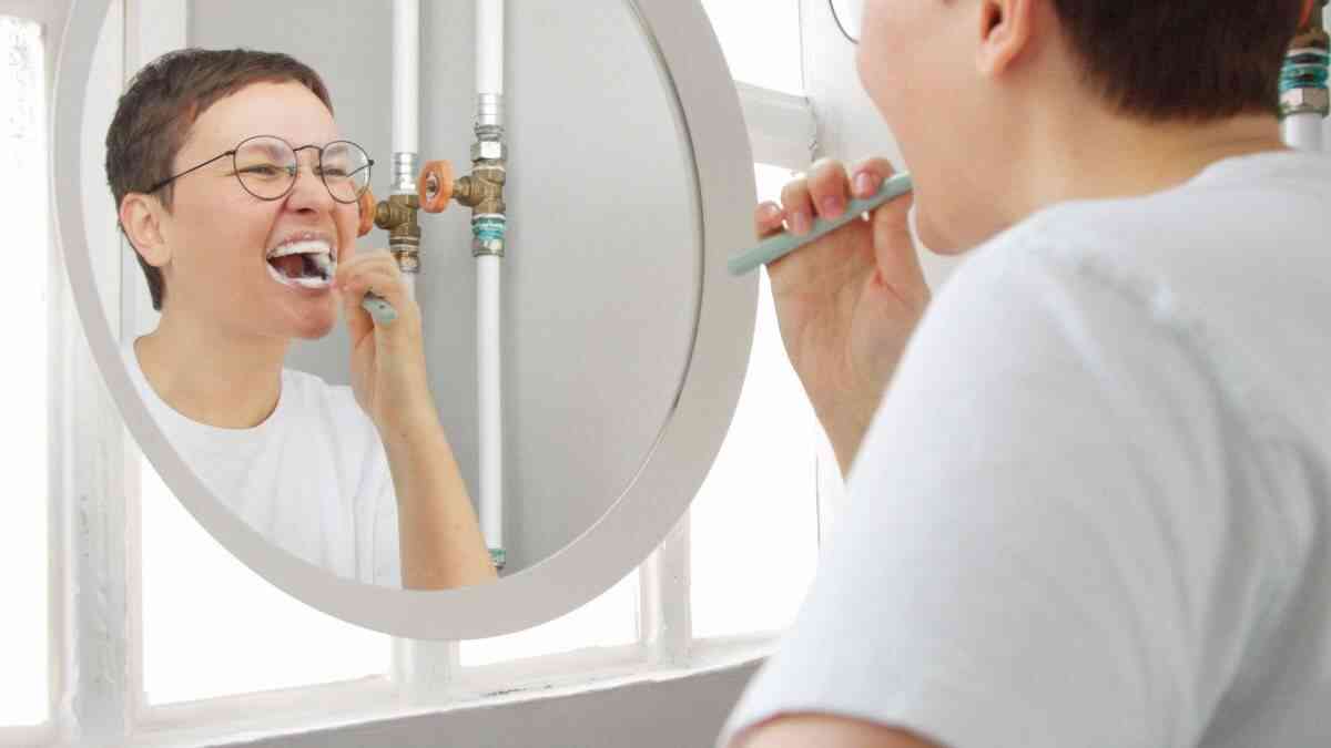 Person brushing teeth while looking in a mirror, demonstrating daily oral hygiene and dental care routine at home.