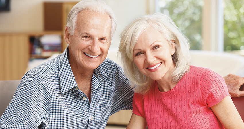 Old couple smiles with new dental implants while sitting together on couch